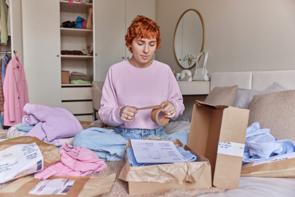 Online selling and shopping concept. Redhead European woman packs clothes in carton boxes prepares