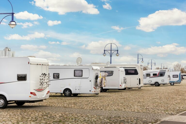 Many white modern campervan recreational motor home vehicles parked in row at camper park site